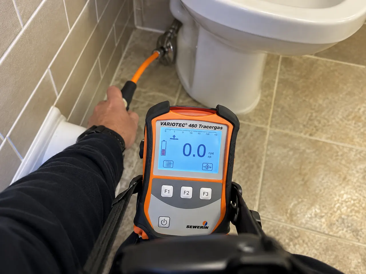 Tracer gas detector held near a bathroom supply line during indoor water leak detection